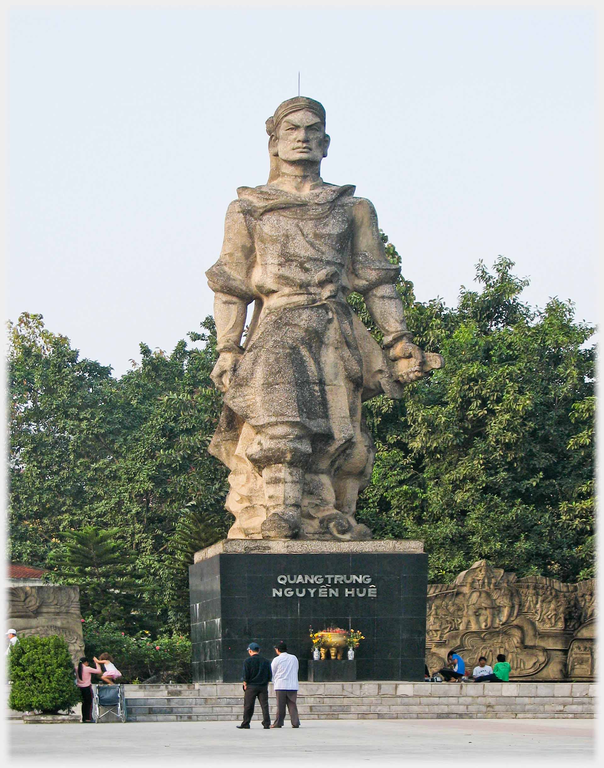 Large statue on black plinth with people below.