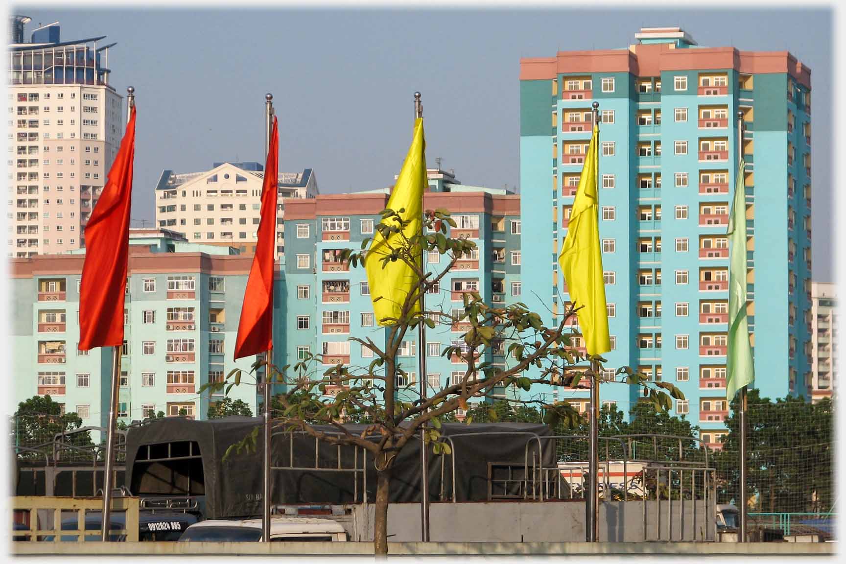 Yellow and red flags hanging in front of turquoise tower blocks.