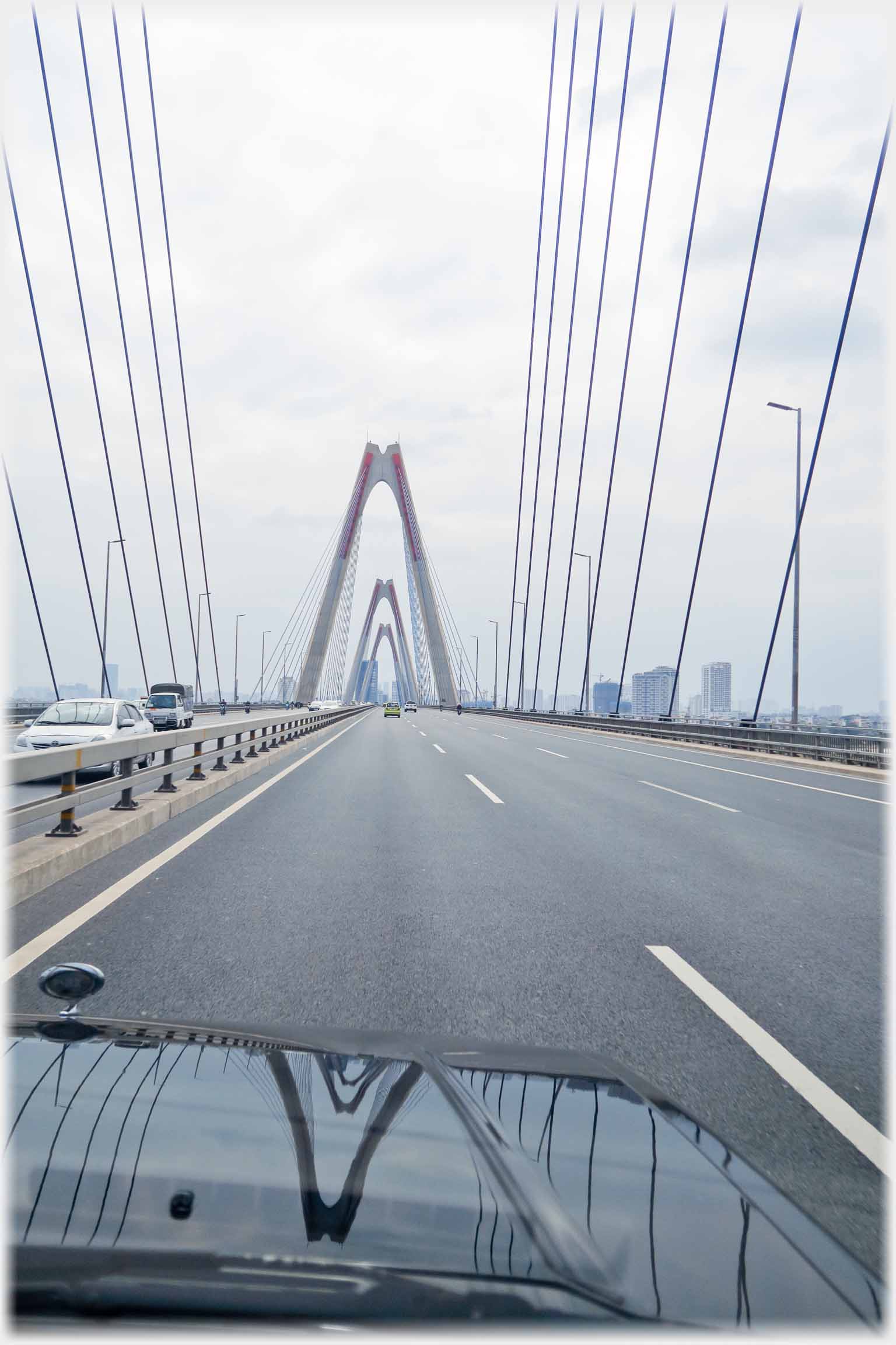 Carriageway with suspension cables dropping from the supporting columns, and car bonnet.