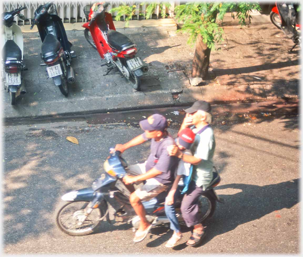 Two adults with child between them on motorbike.