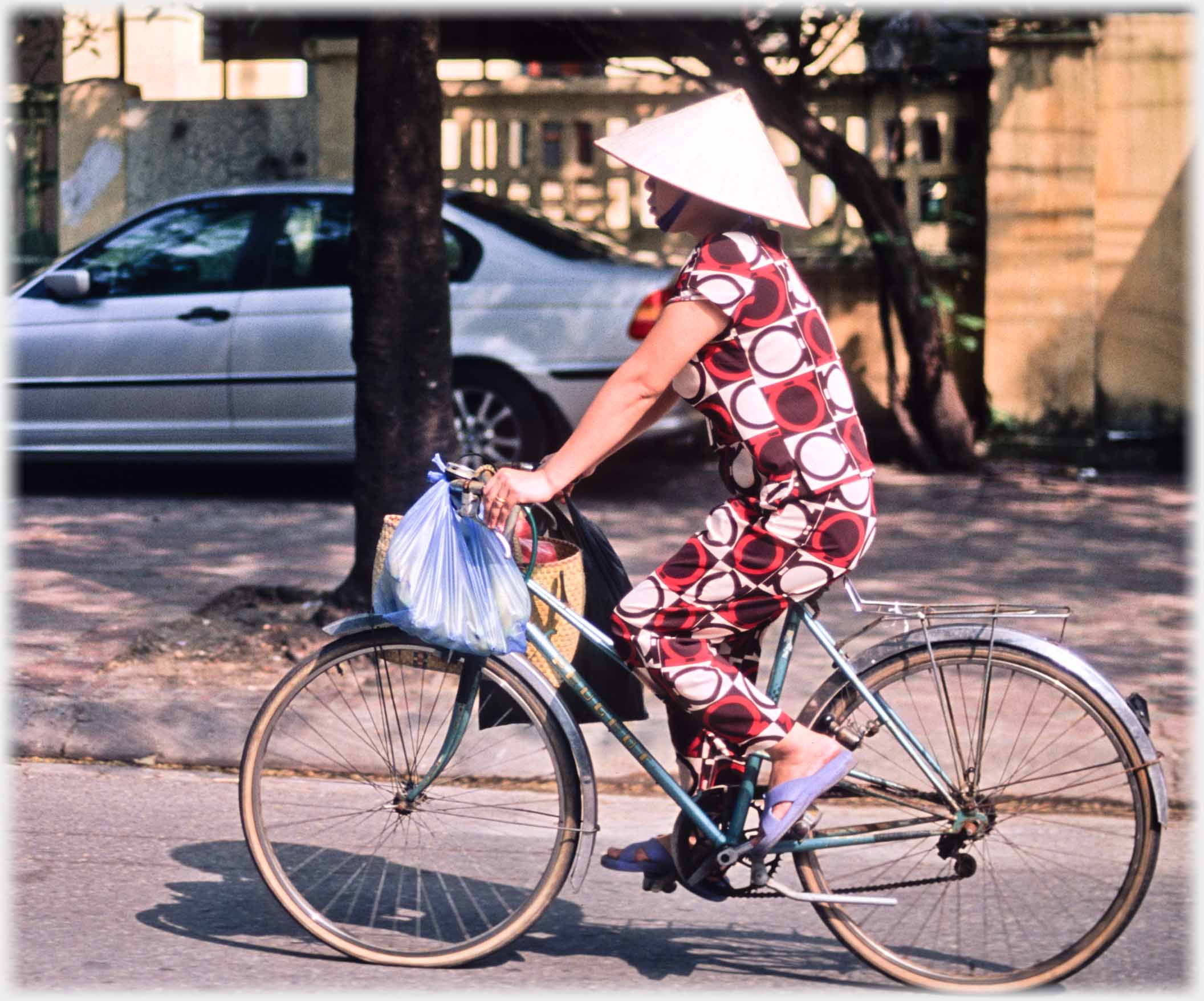 Woman on cycle with bags and hat.