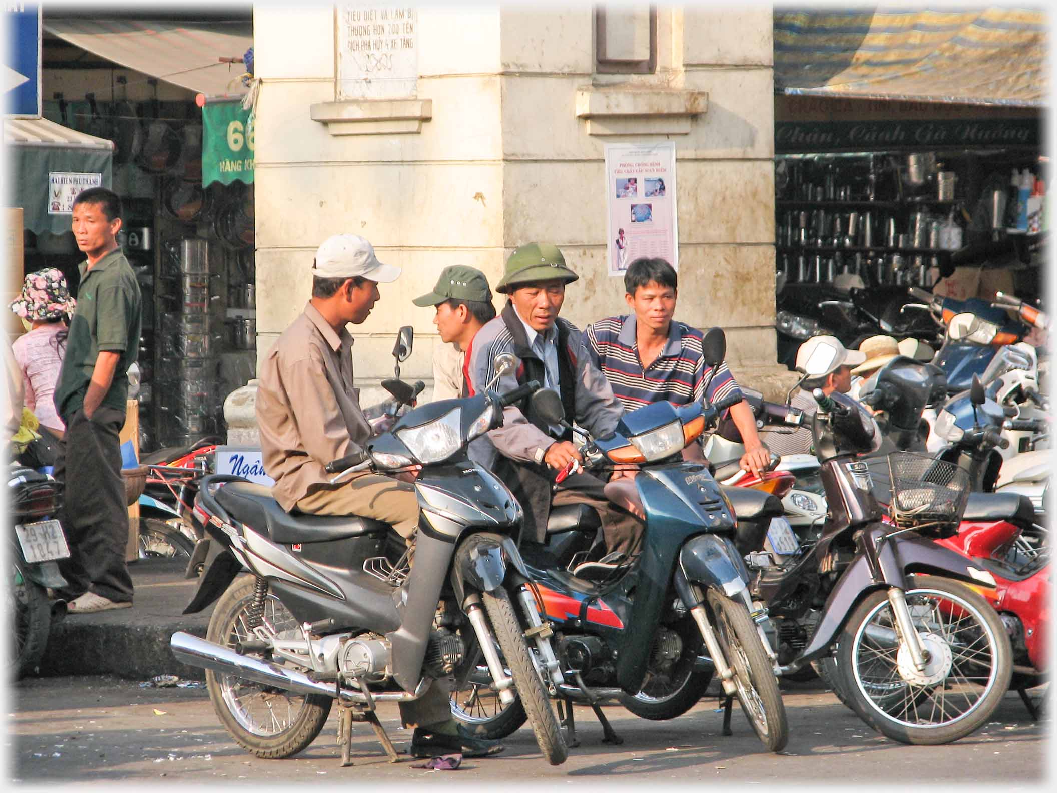 Three men on parked motorbikes talking.