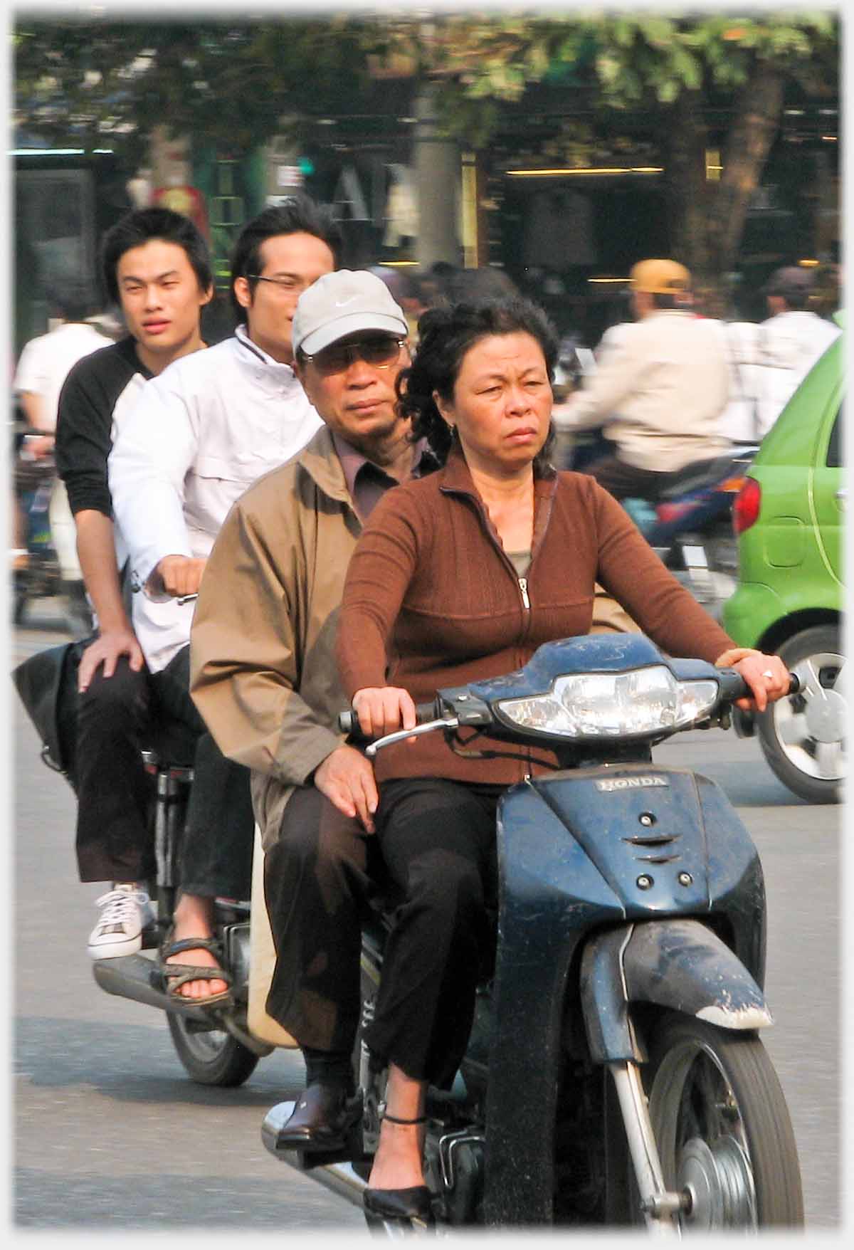 Woman driving motorbike with man as pillion.