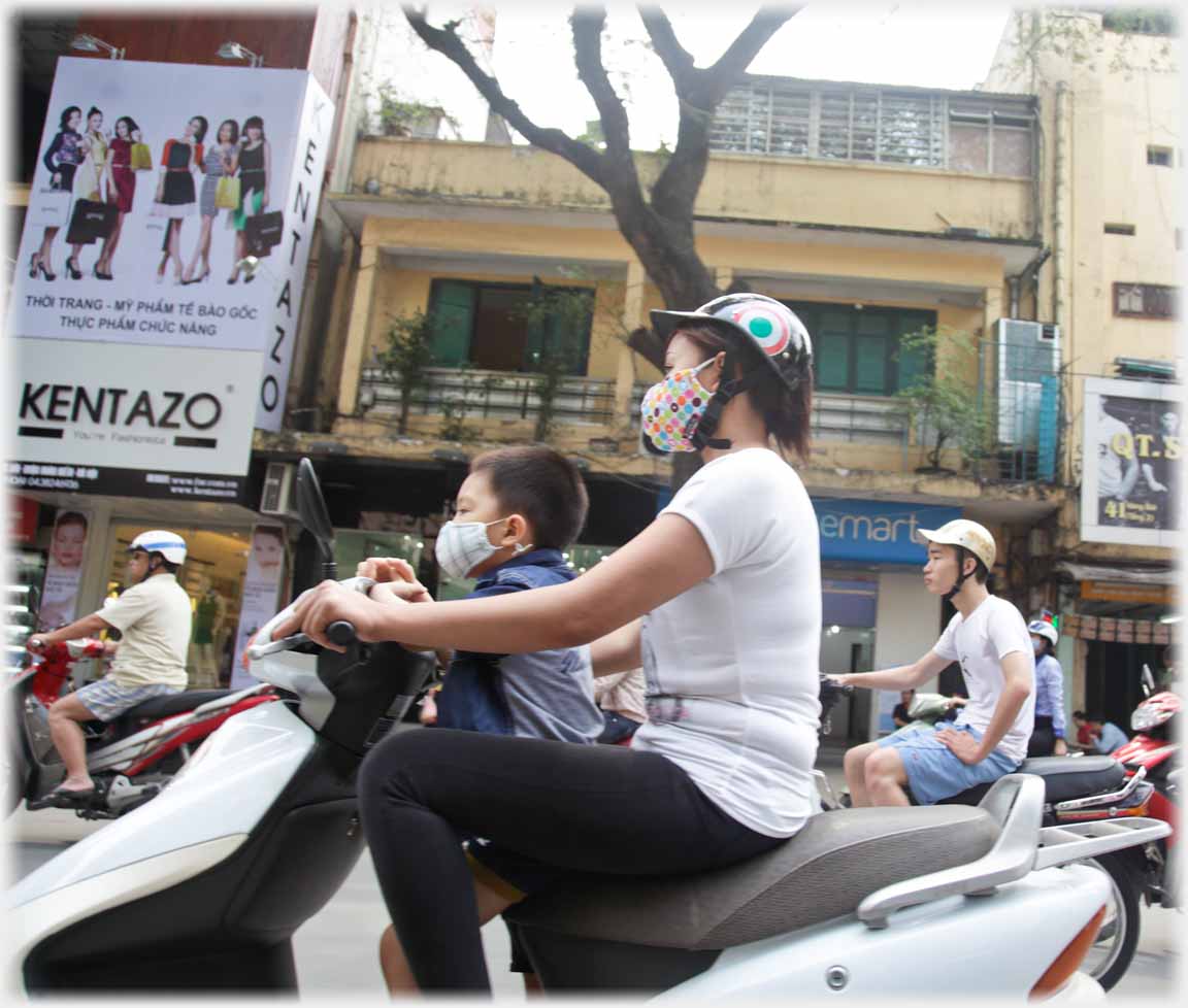 Woman with child standing on scooter floor in front of her.