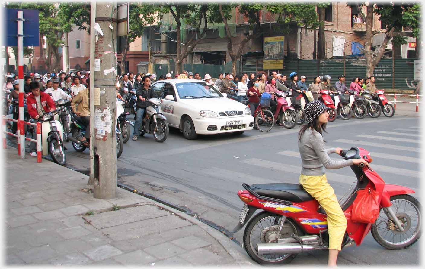 Woman on motorbike sitting at right angles to a line of traffic waiting for lights.