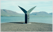 Large sculpture like a fish's tail with mountains and water beyond.