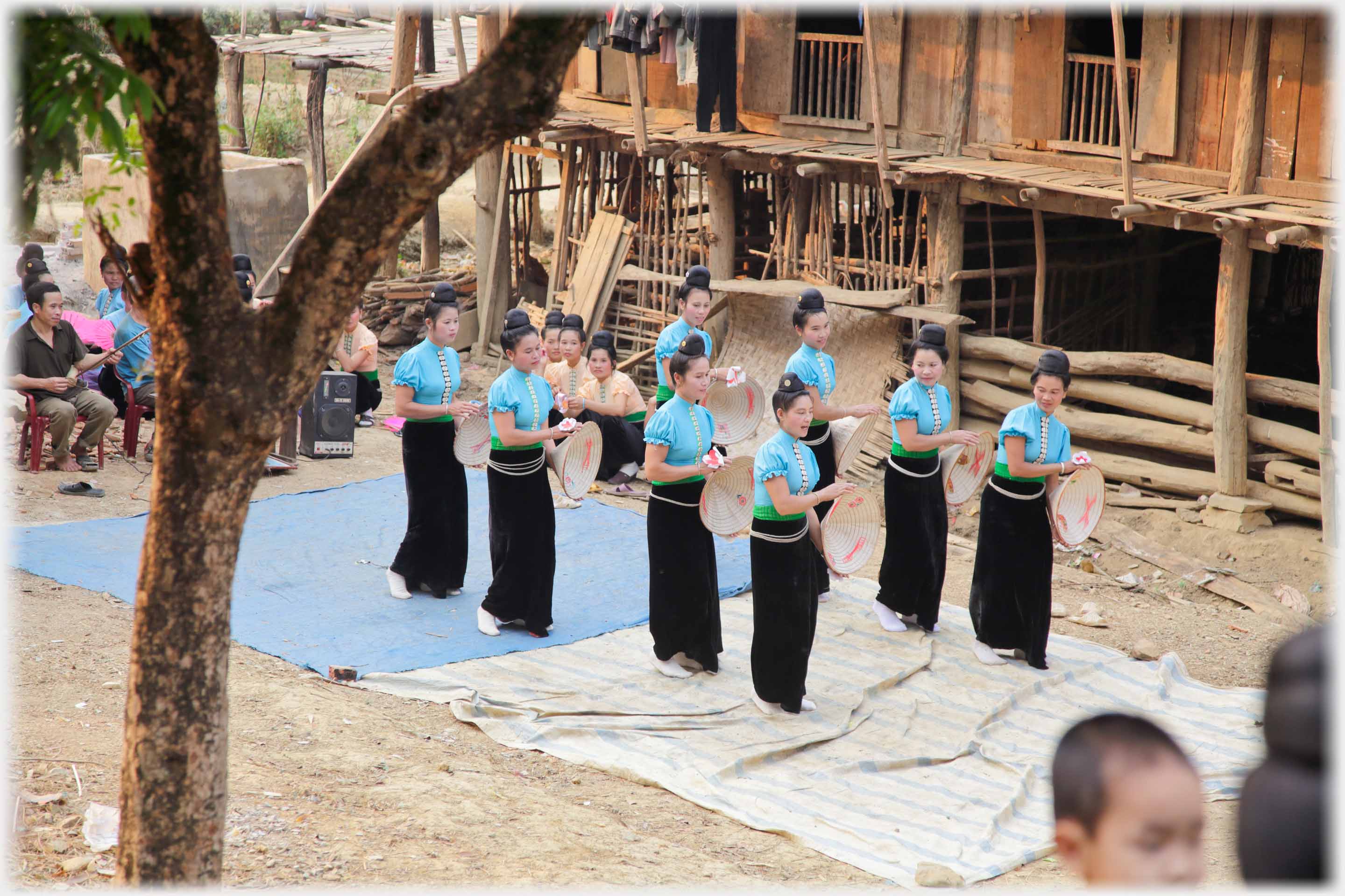 Two lines of women in long black skirts holding conical hats.