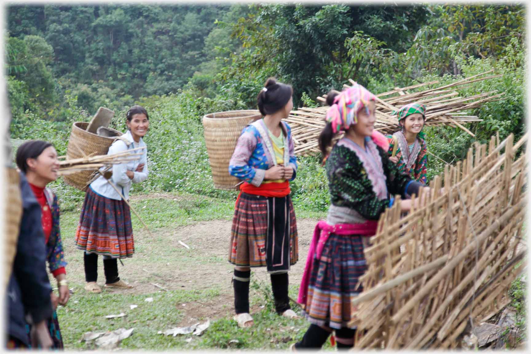 Women with back packs and wattle fencing.