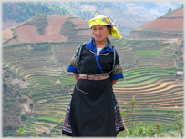 Woman in colourful garb squatting examing produce in a basket.