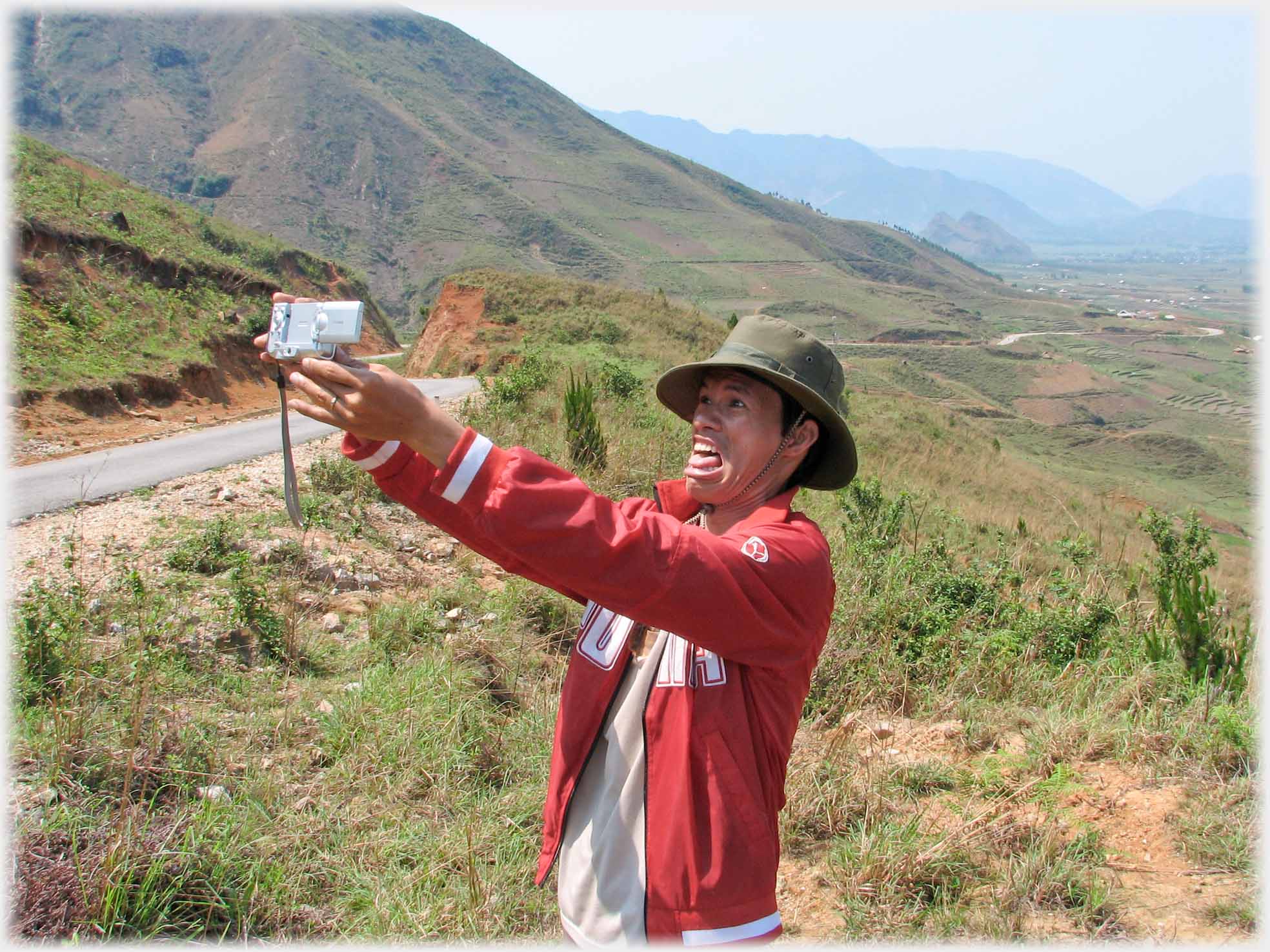 Han in hat holding up camera to take photo f himself, tongue out.