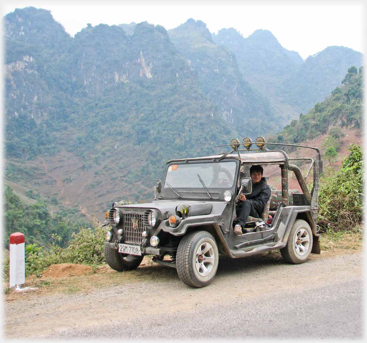 Jeep on road with line of karst hills behind.