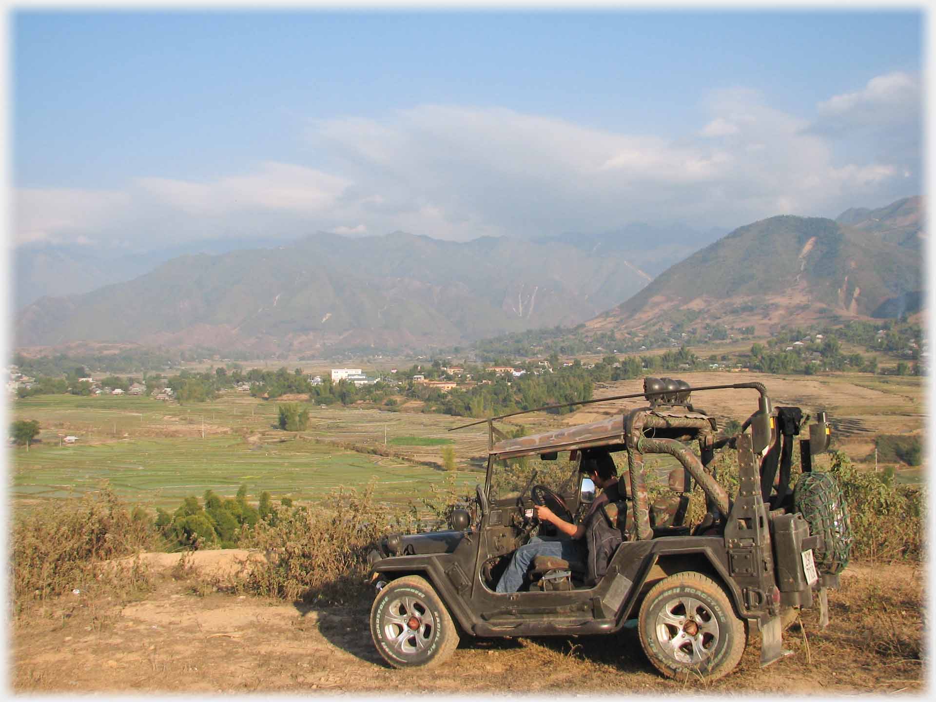 Jeep parked on hill overlooking valley and hills.