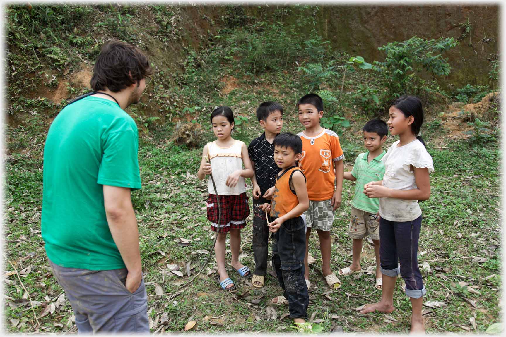 Western man leaning towards group of slightly perplexed looking children.