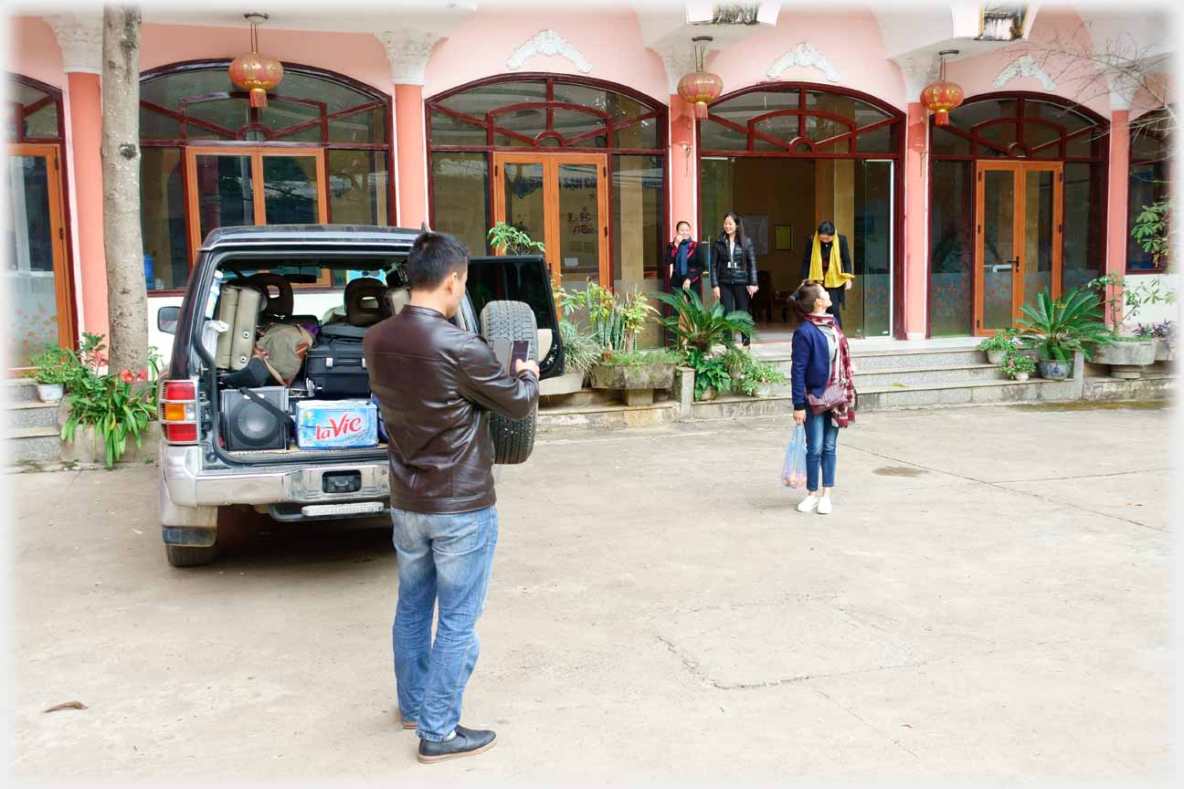 Courtyard with vehicle and man taking photo of woman looking back at building facade.