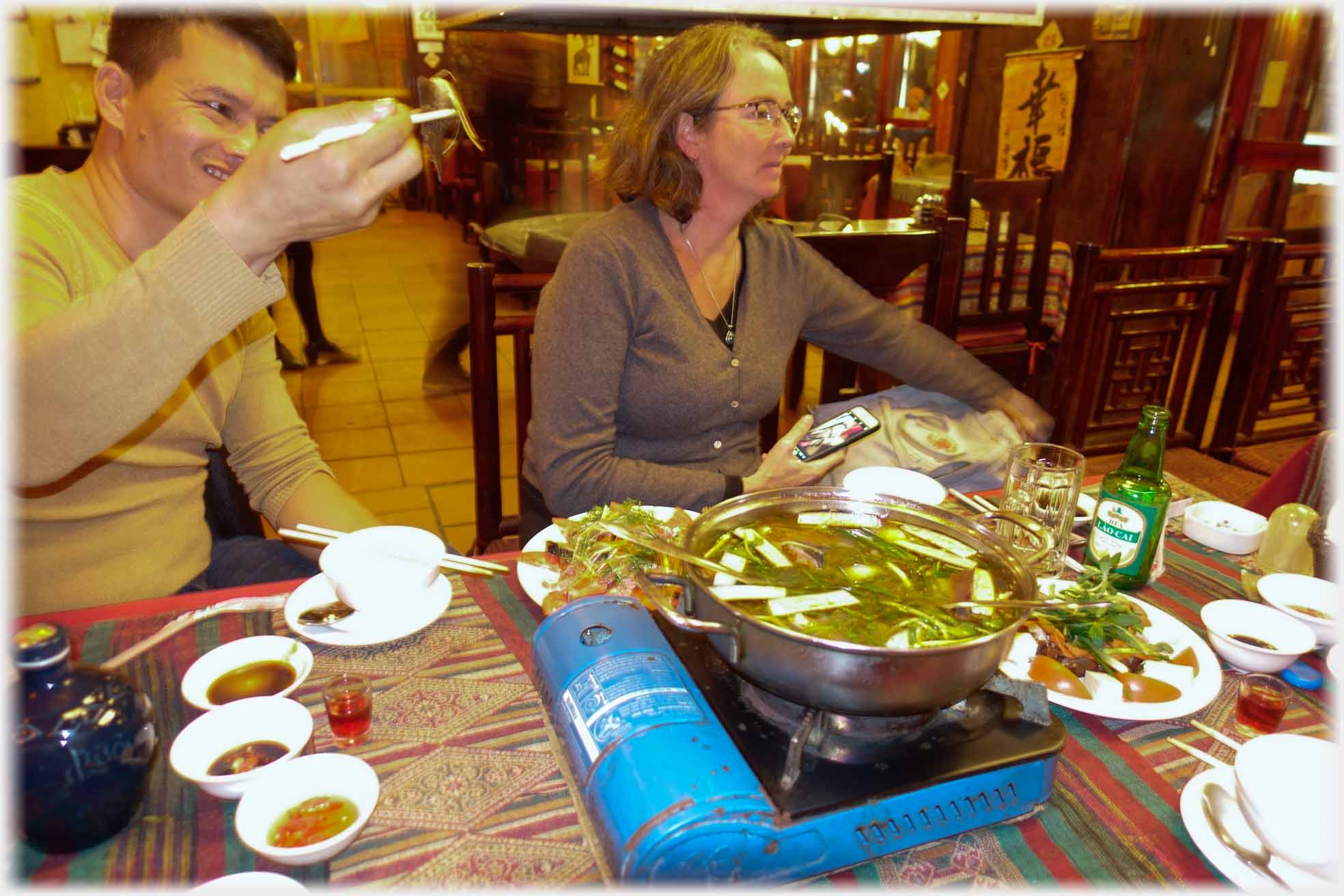 Table with food and single gas ring with large vessel on it. Han holding up an item.