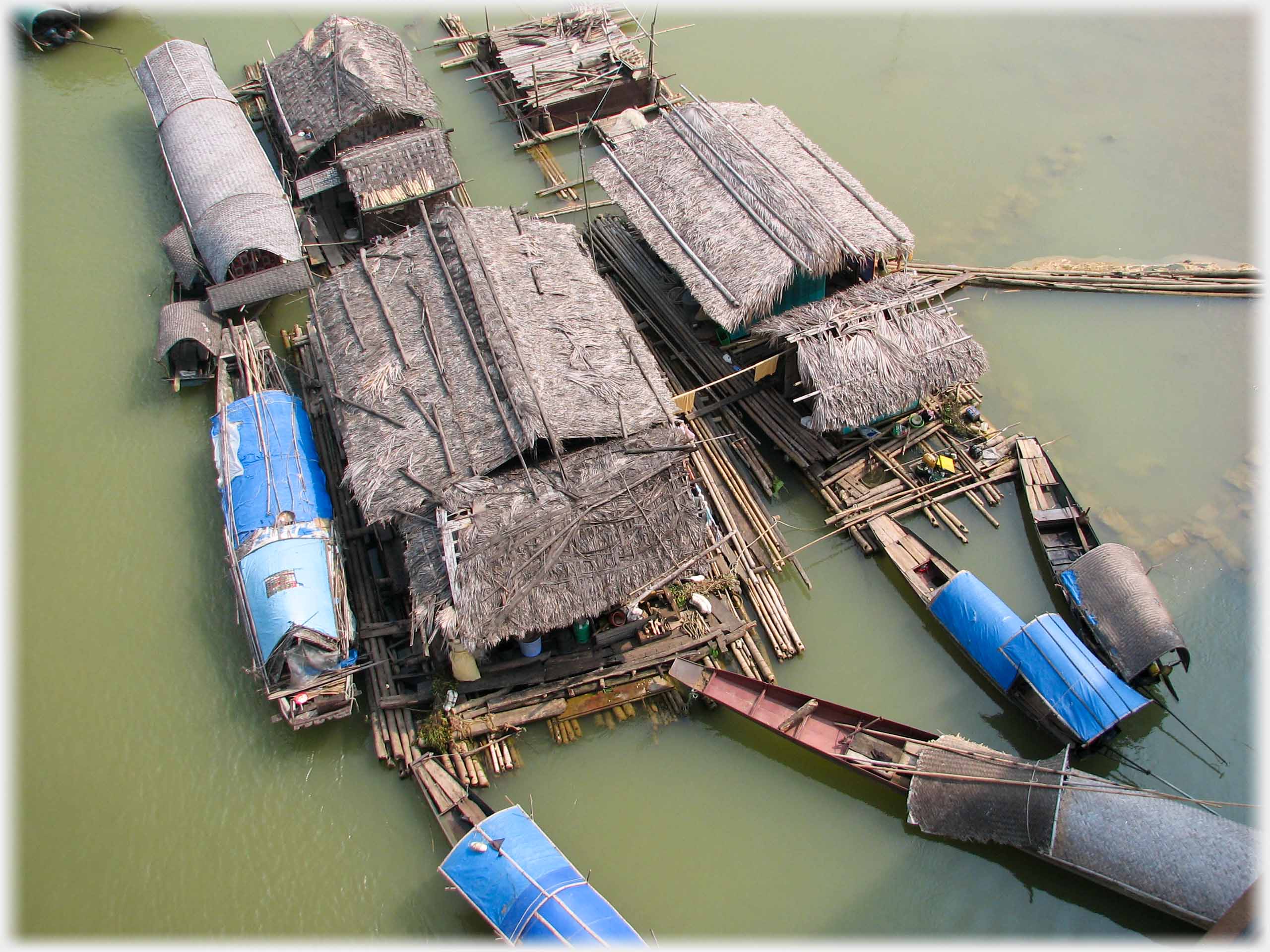 Looking down on the thatched and taupaulin coveredd roofs of a group of houseboats.