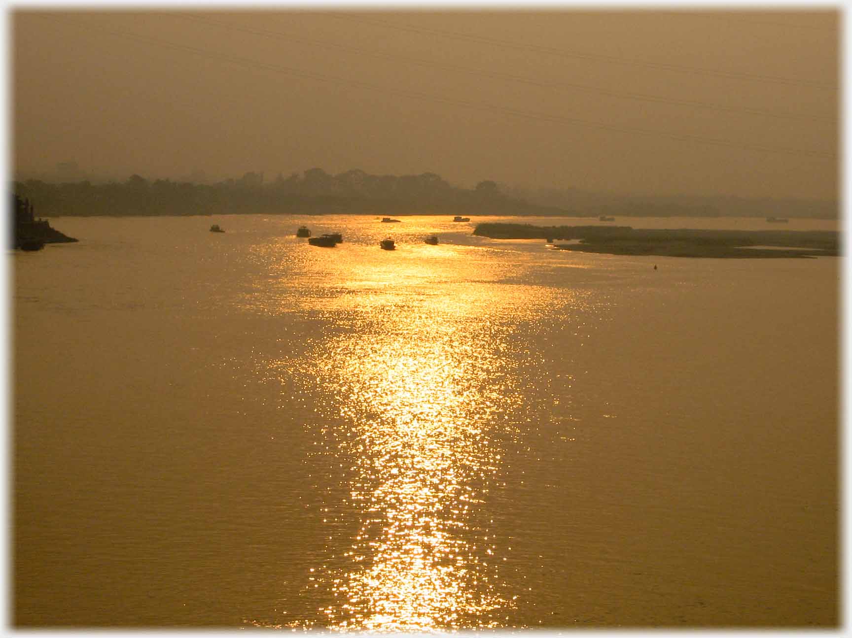 Sun running in band towards the camera across river, boats in distance.