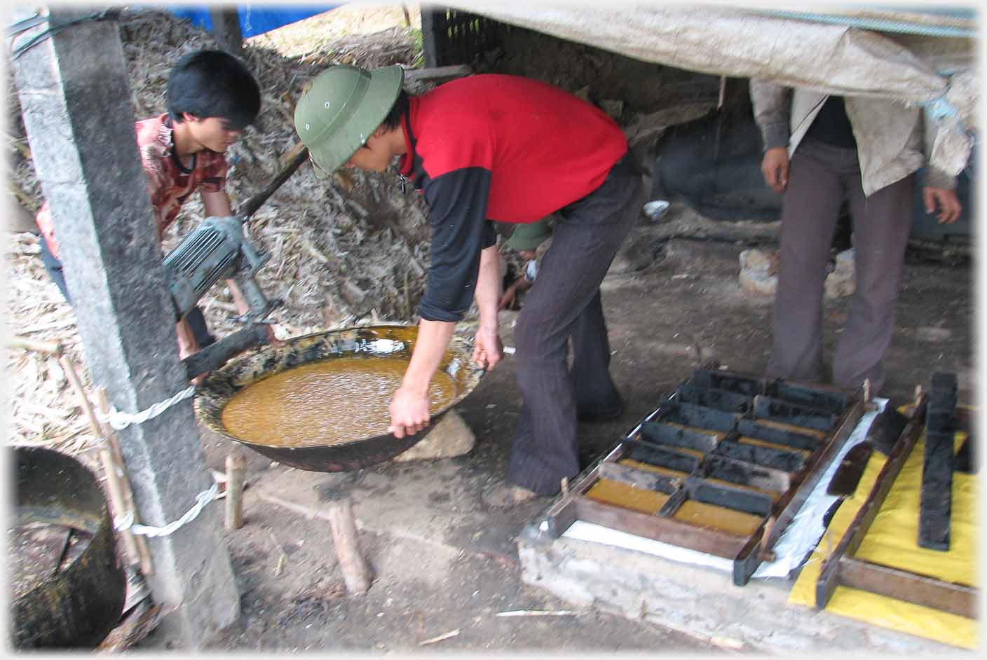 Two men carrying one of the woks of melted sugar.