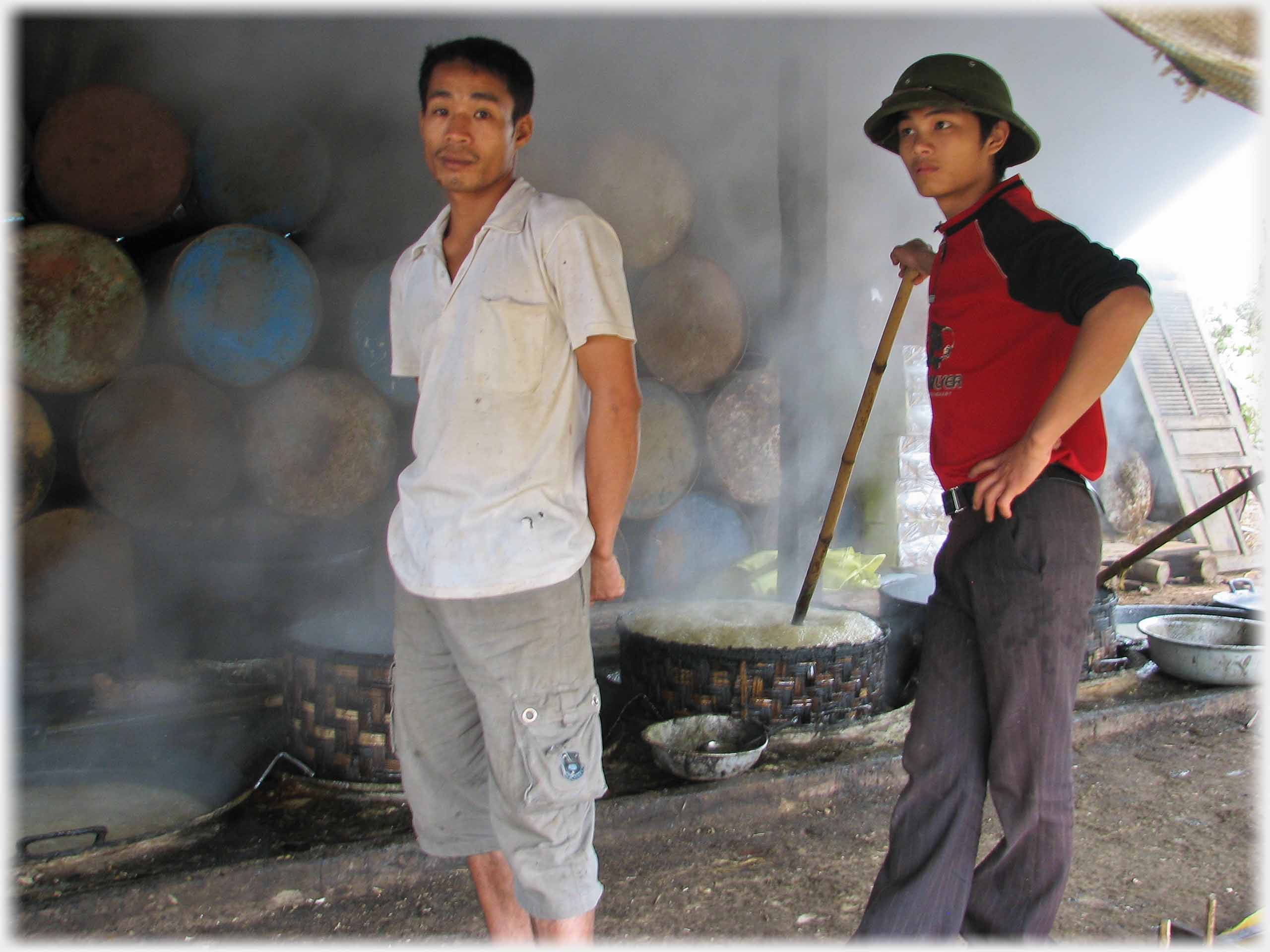 One man standing looking at the camera, another leaning on a pole in a vat.