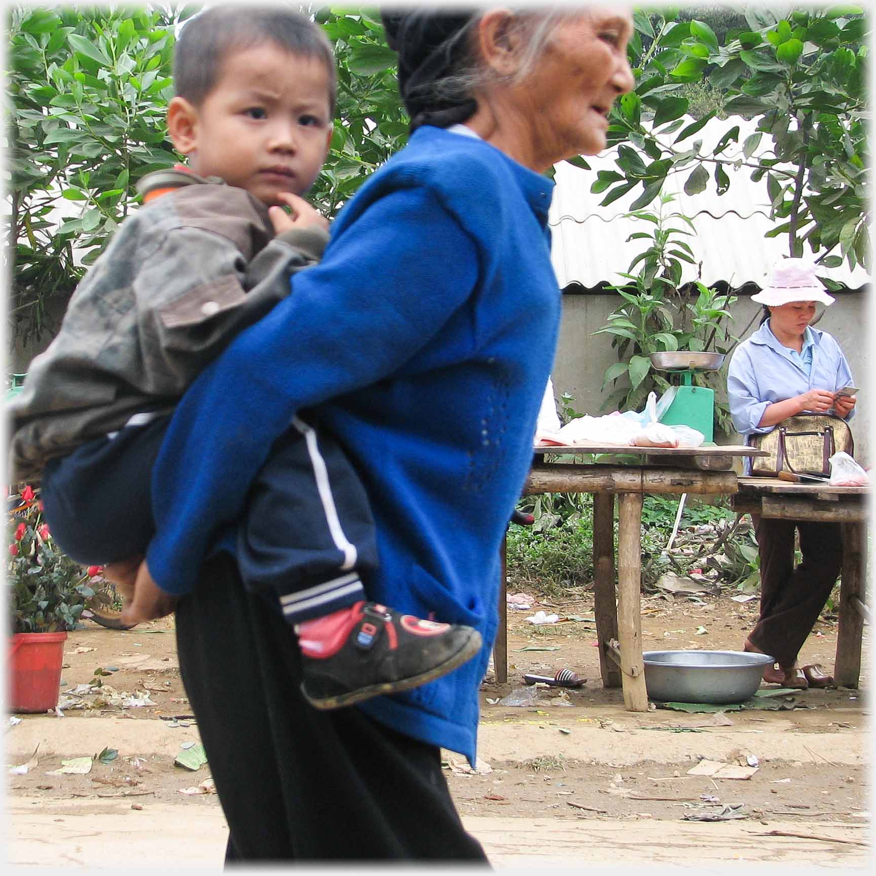 Woman carrying substantial three-year old on her back.