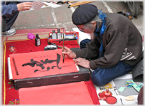 Man in beret writing with brush.