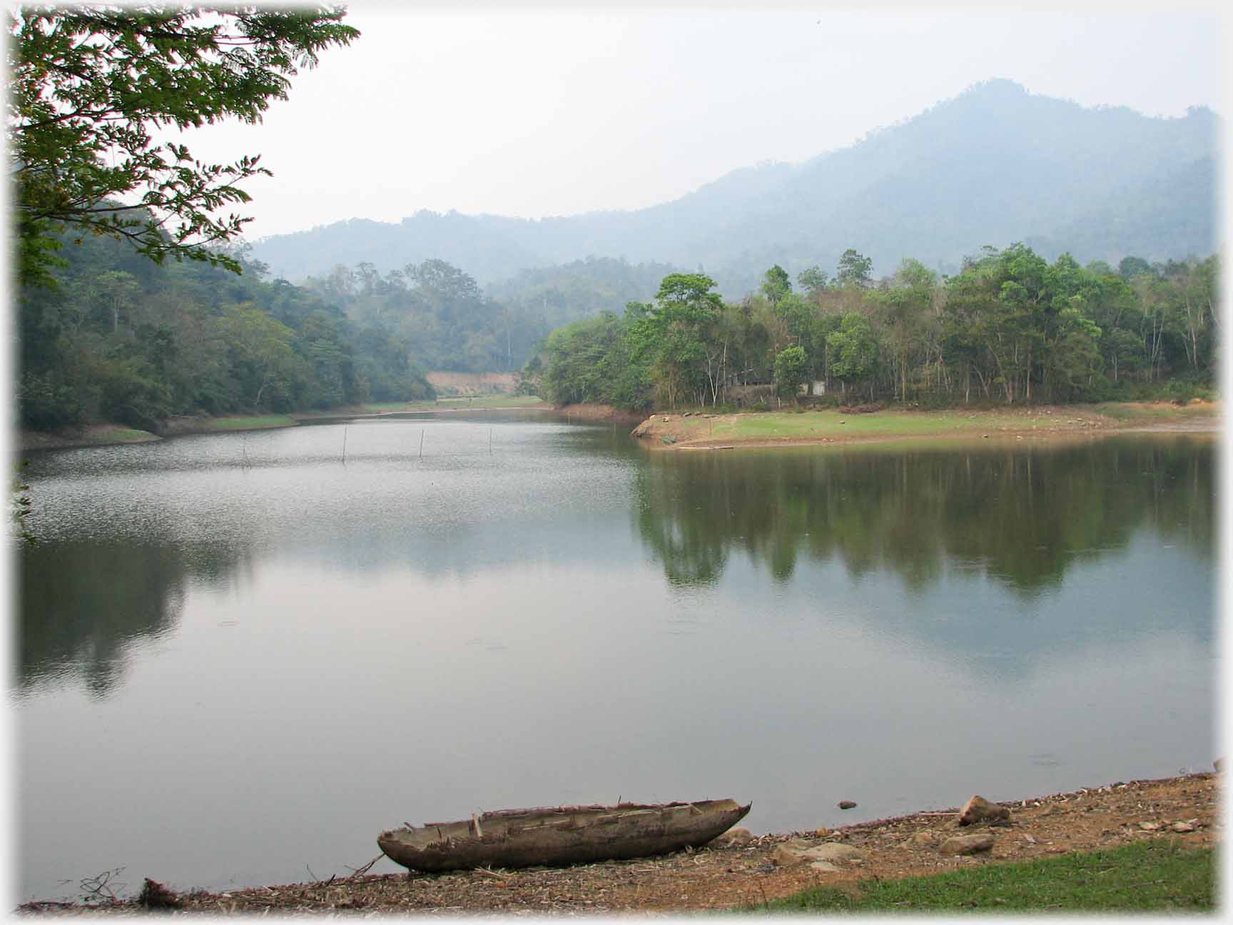 Lake wiht reflected trees, hill and dugout canoe in foreground.